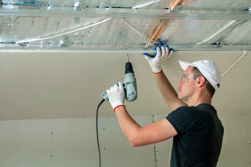 Montážnik upevňuje stropný panel pomocou elektrického náradia